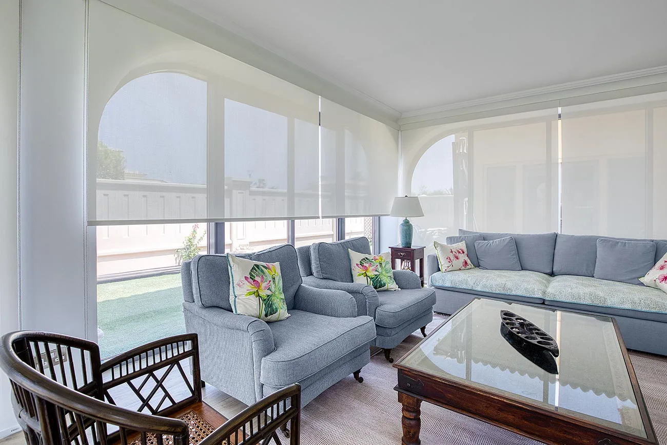 Beige sunscreen roller blinds covering floor-to-ceiling windows in an Abu Dhabi office space.